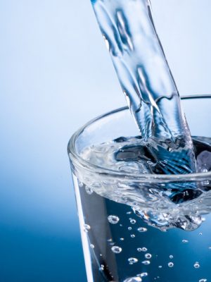 Pouring water into glass on blue background