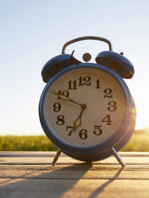Retro alarm clock on wooden table in garden against sky