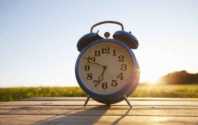Retro alarm clock on wooden table in garden against sky